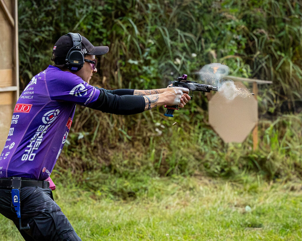 Zawodnik IPSC podczas strzelania sportowego na strzelnicy, wystrzał z lufy pistoletu fotografia strzelecka